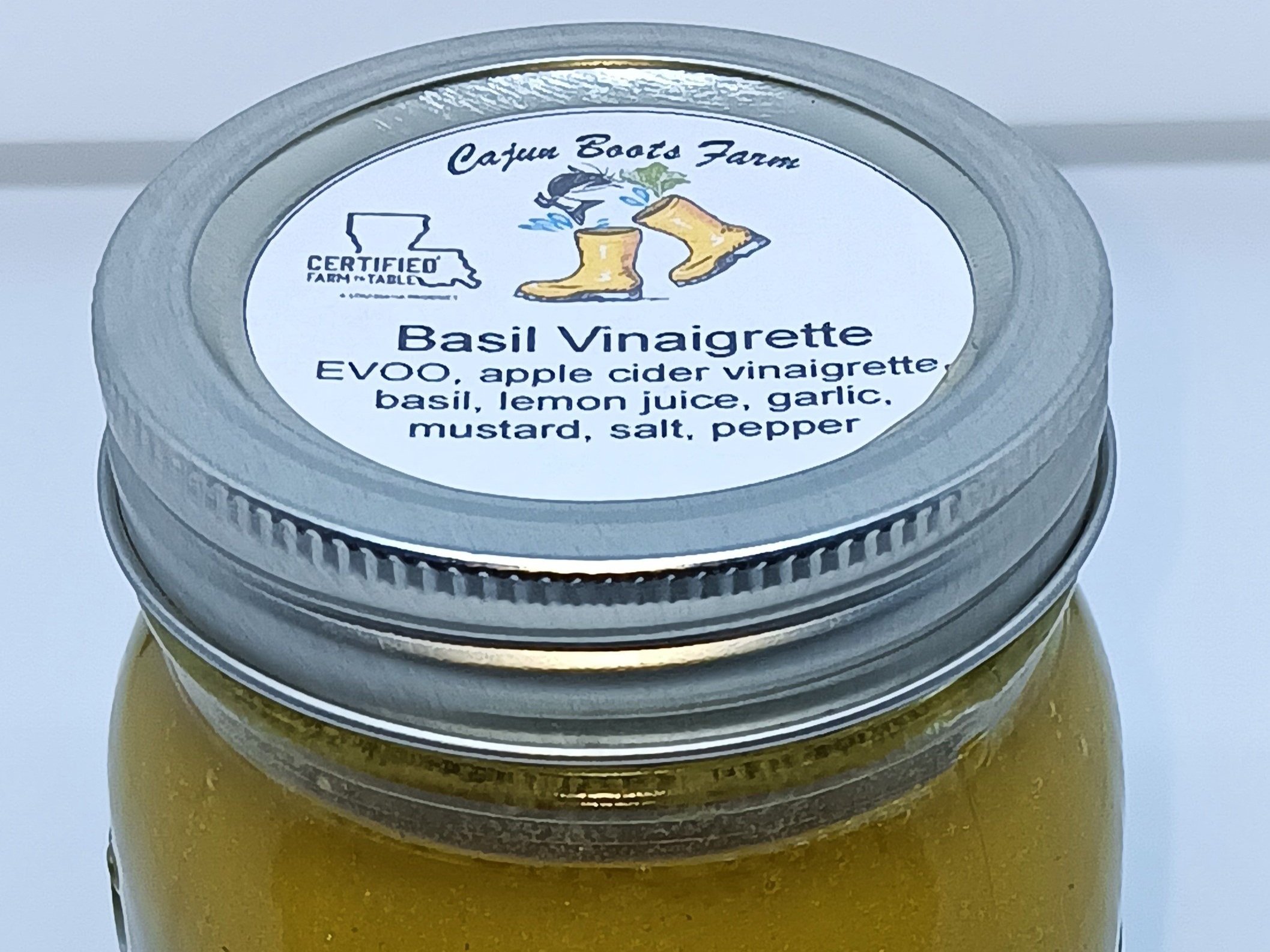 Basil vinaigrette in a jar from Cajun Boots Farm, featuring ingredients like extra virgin olive oil, apple cider vinegar, basil, lemon juice, garlic, mustard, salt, and pepper. Ideal for salads and enhancing dishes.