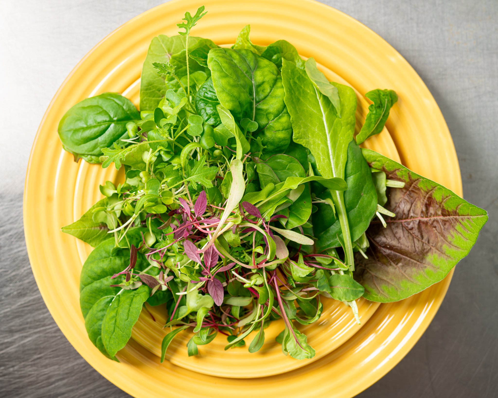 Fresh mixed greens including spinach, arugula, and microgreens arranged on a vibrant yellow plate, showcasing a healthy and colorful salad option.